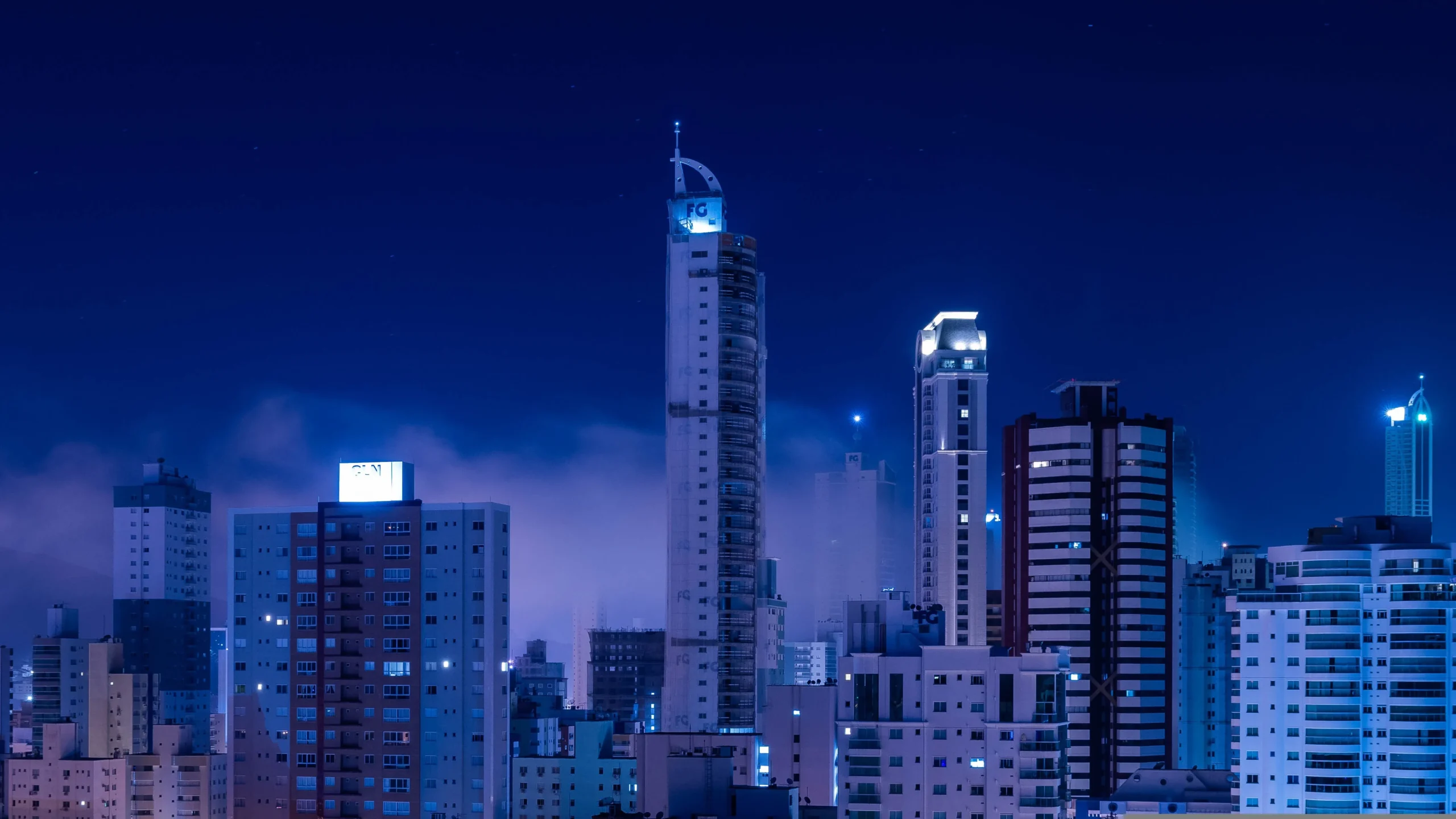 Vista panorâmica noturna de Balneário Camboriú, destacando seus arranha-céus iluminados, a orla da praia e a vida noturna intensa da cidade.
