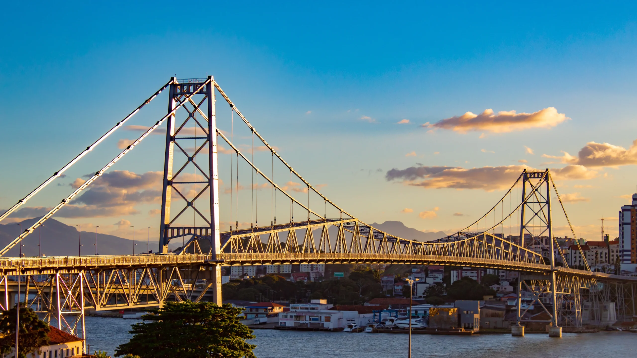 Imagem realista de Florianópolis, destacando a icônica Ponte Hercílio Luz, infraestrutura moderna e qualidade de vida na capital catarinense.